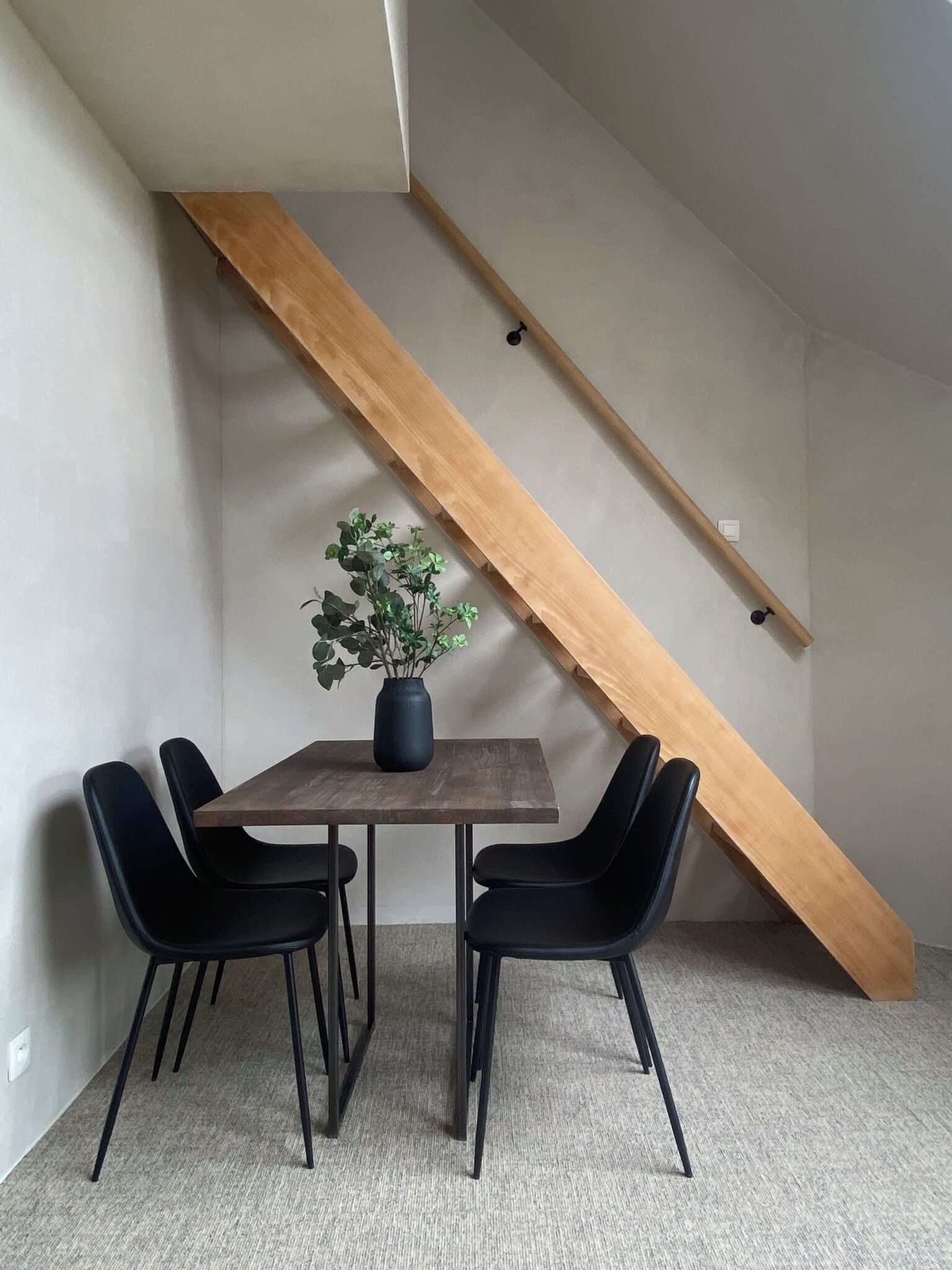 A dining area with a wooden table, four black chairs, a potted plant, and a slanted ceiling.