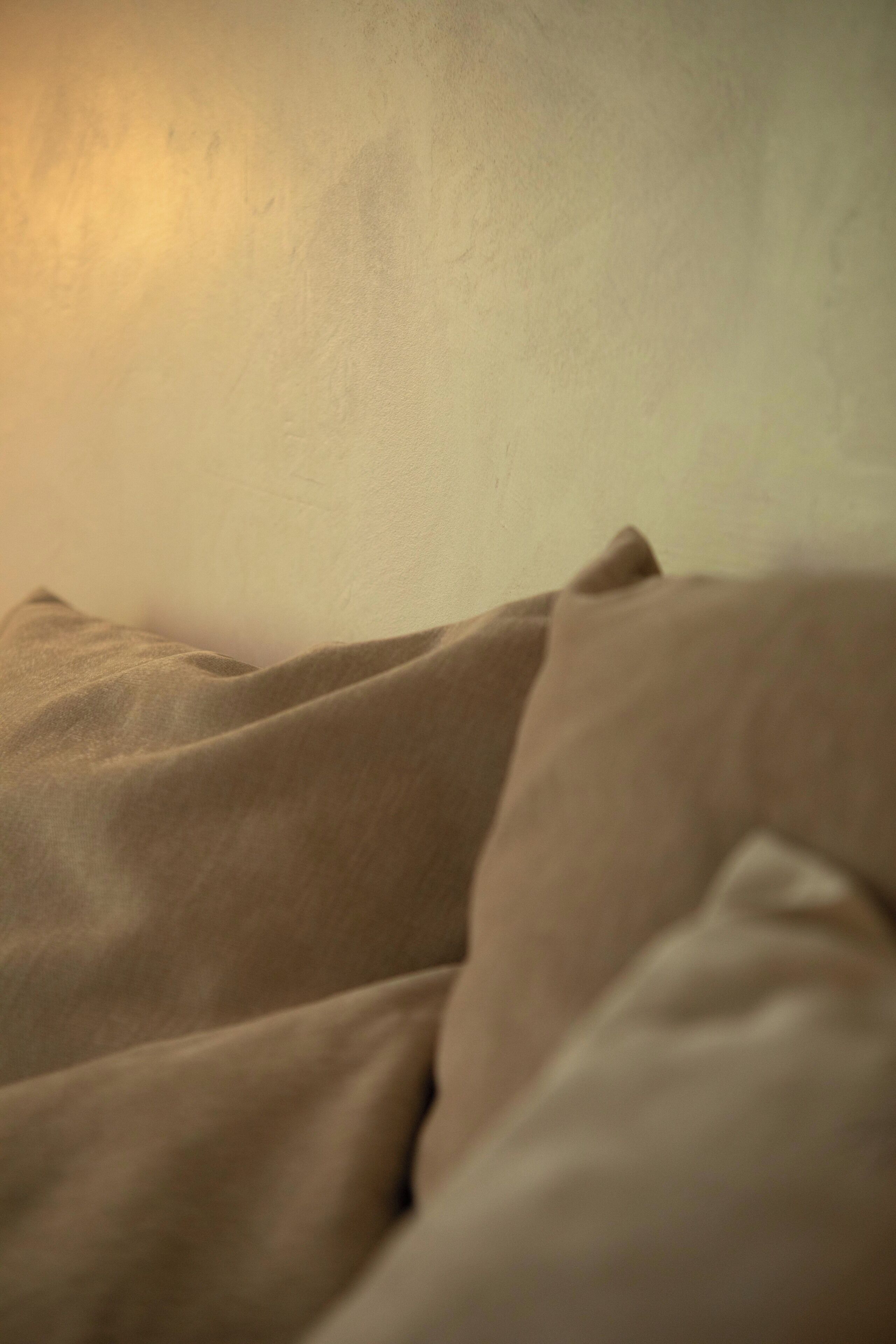 A close-up of a textured fabric, possibly a bedspread or blanket, with a soft, warm light source in the background.