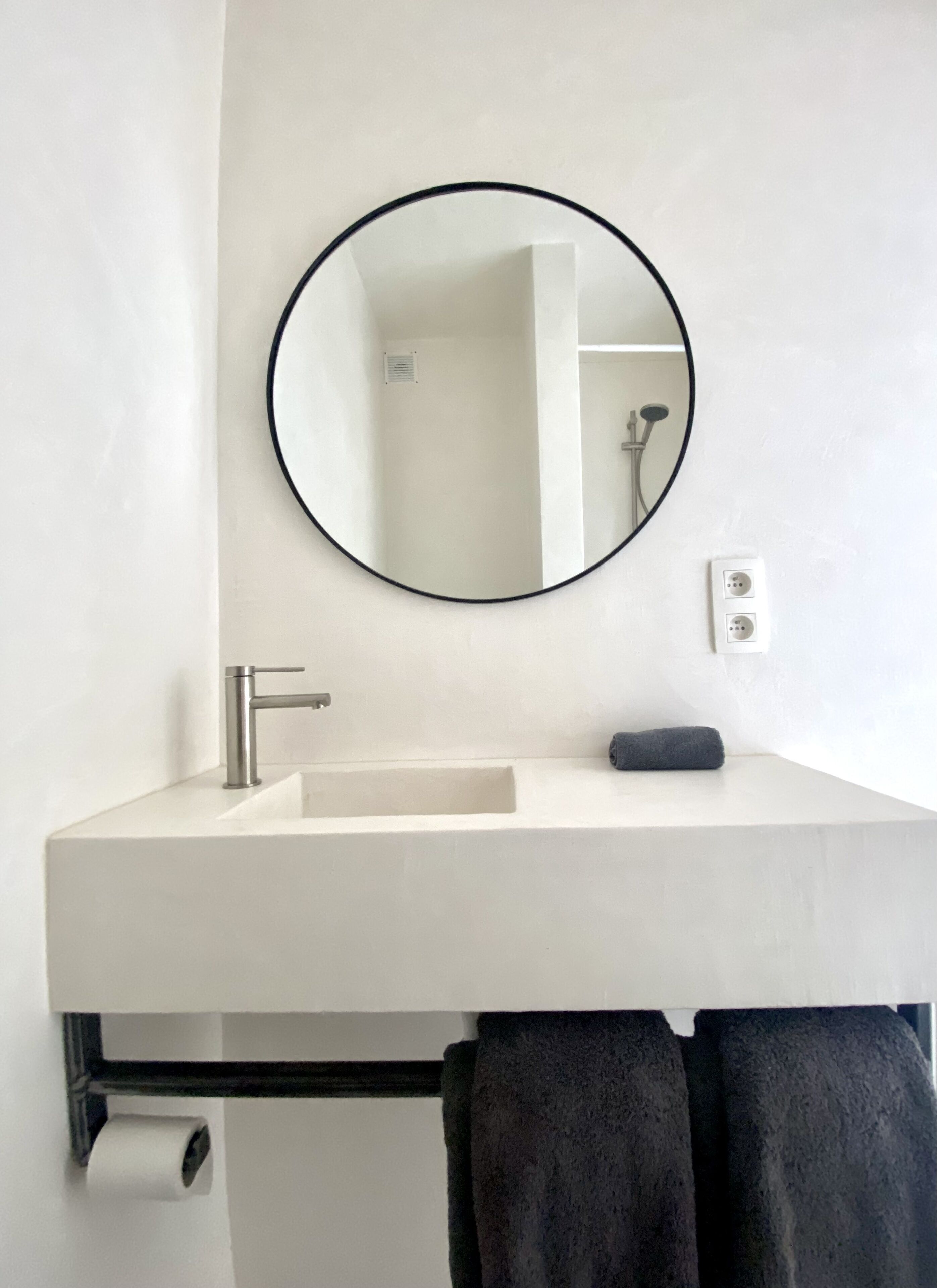 A bathroom with a white sink, a round mirror, a towel, and a toilet paper holder.