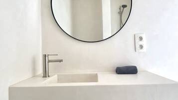 A bathroom with a white sink, a round mirror, a towel, and a toilet paper holder.