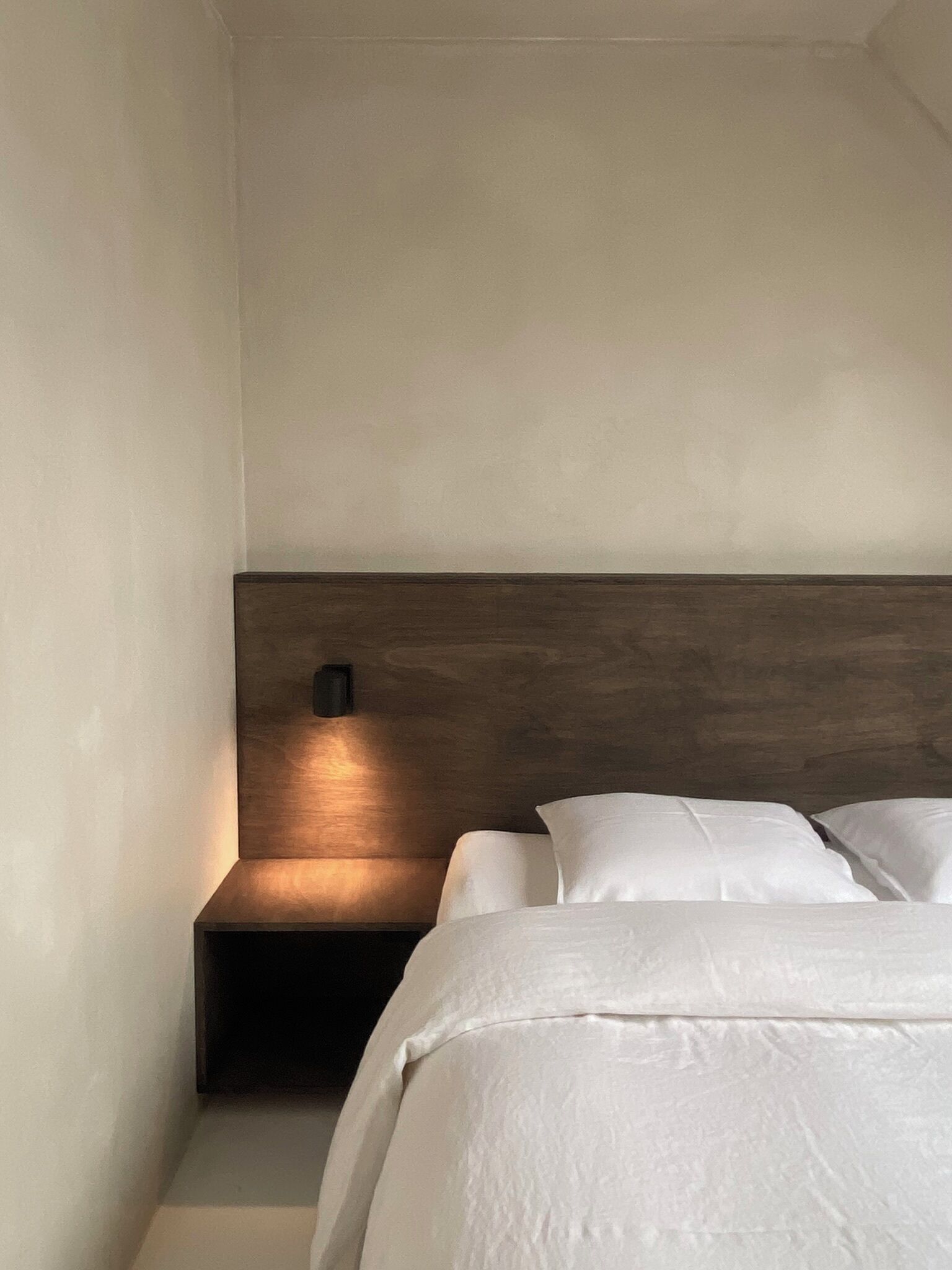 A bedroom with a wooden headboard, a bedside table, and a wall-mounted light.