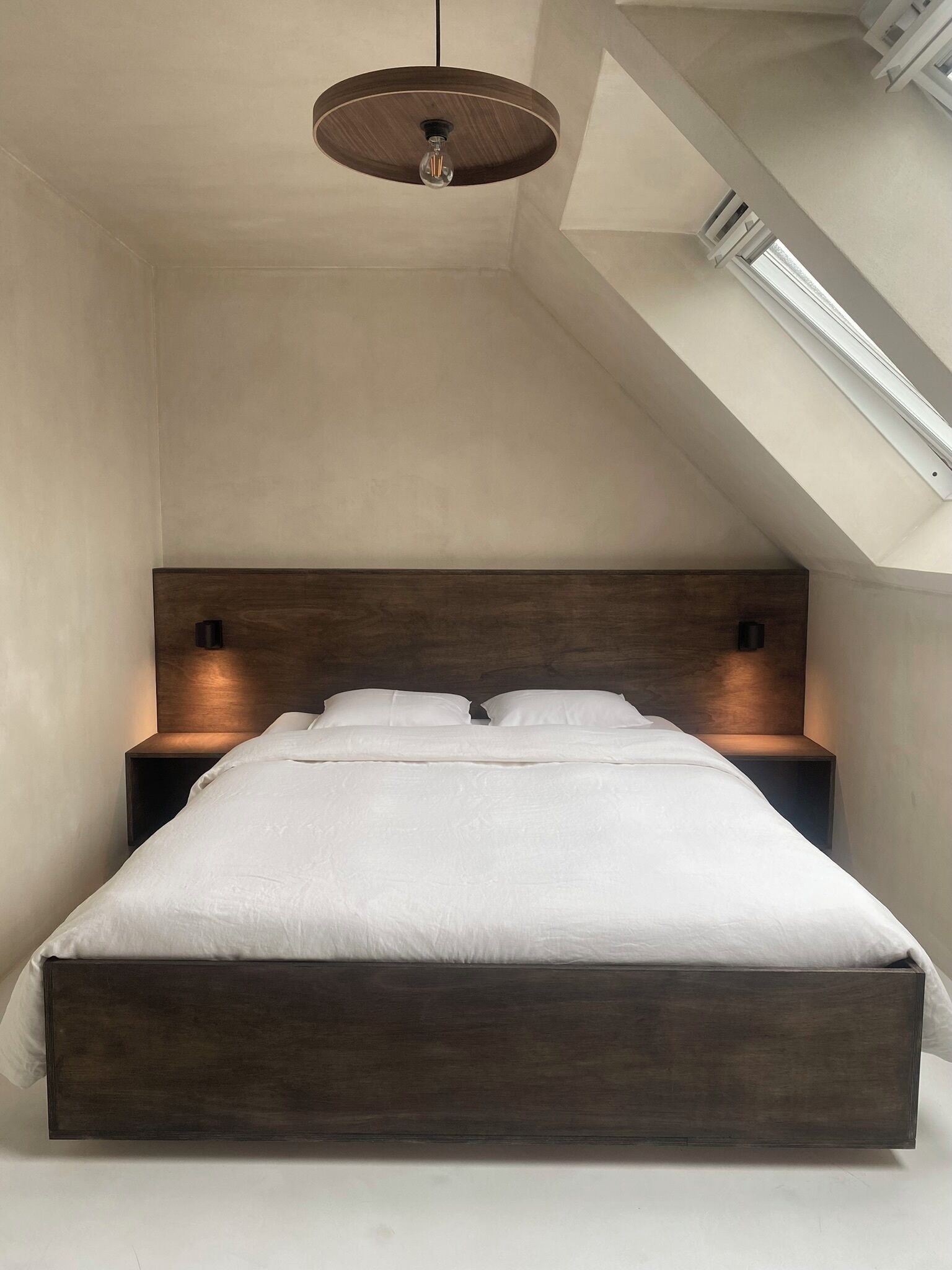 Una camera da letto moderna con soffitto spiovente, un lampadario al centro e due abat-jour, oltre a una testiera in legno.