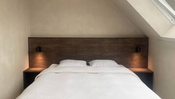 Una camera da letto moderna con soffitto spiovente, un lampadario al centro e due abat-jour, oltre a una testiera in legno.