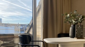 A modern room with a large window, a round table, a black chair, a vase with green leaves, and a sign on the table.