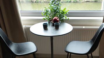 Una habitación con una mesa redonda, dos sillas, una planta en maceta y un cuenco de fruta sobre una mesa de madera.