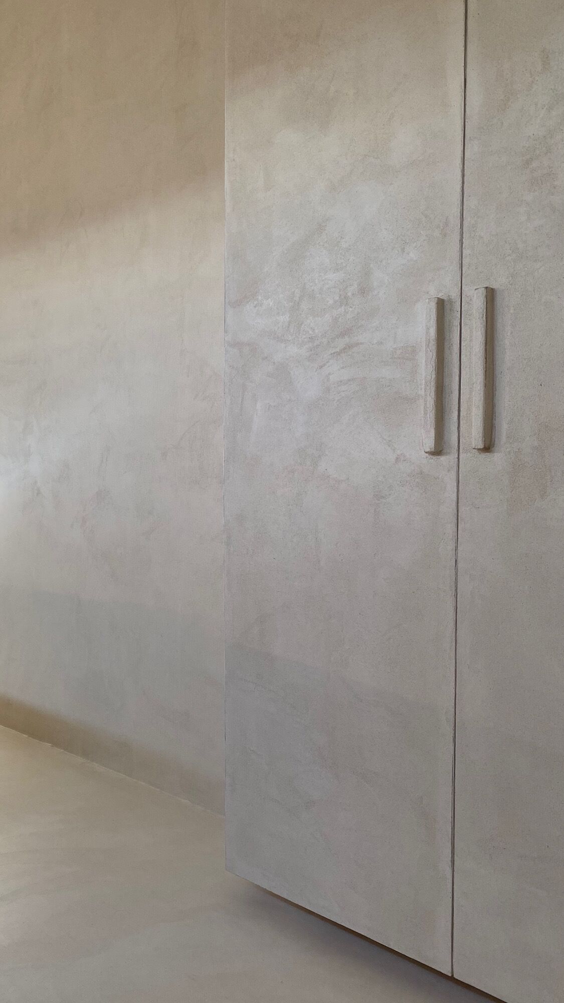 A plain, light-colored wardrobe with two handles.