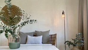 A minimalist bedroom with a bed, pillows, a bedside table with a vase, a floor lamp, and a large woven basket.