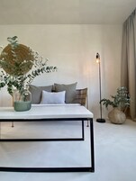 A minimalist bedroom with a bed, pillows, a bedside table with a vase, a floor lamp, and a large woven basket.
