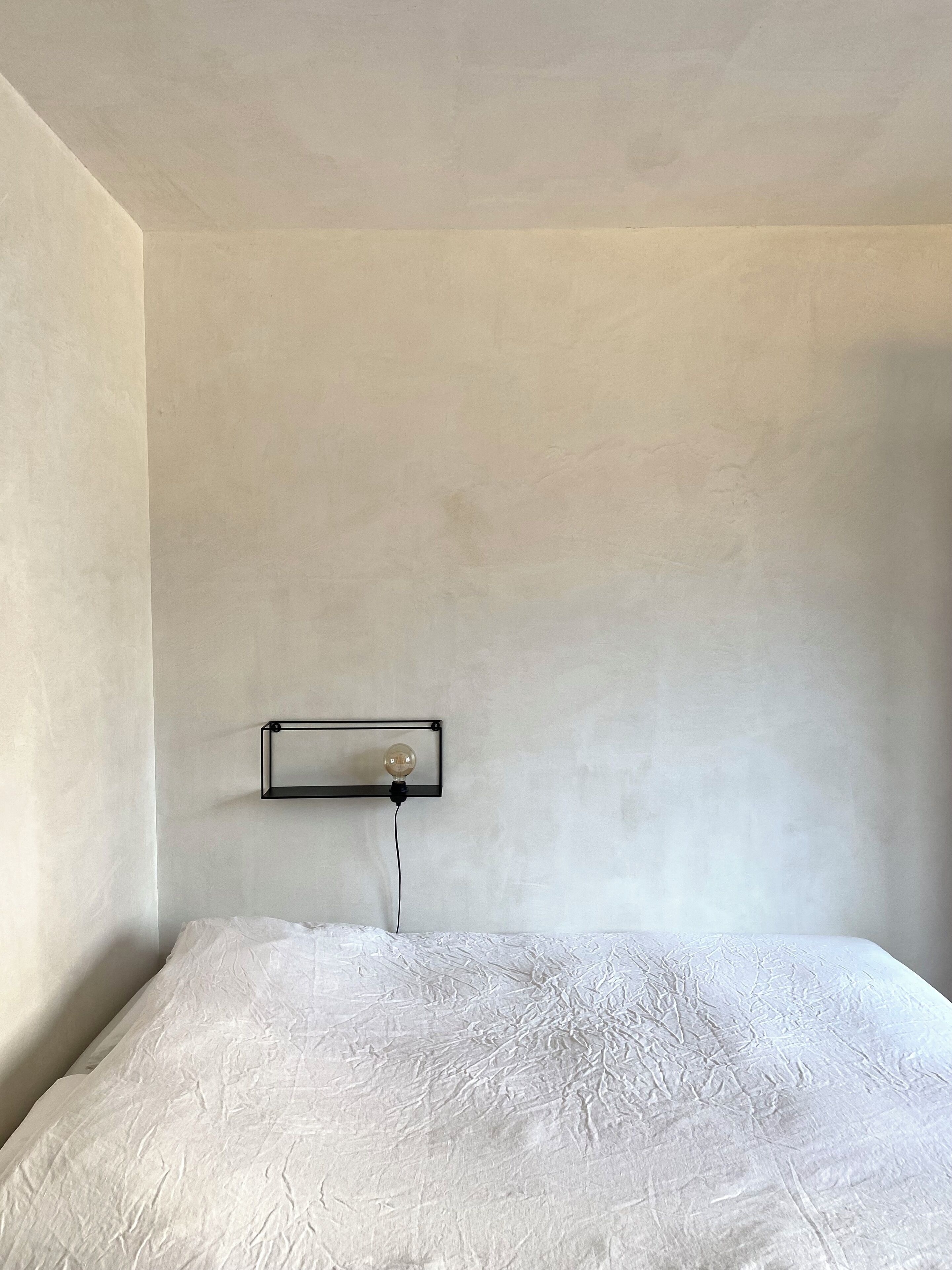 Un dormitorio con una cama individual, una lámpara de pared y paredes lisas.