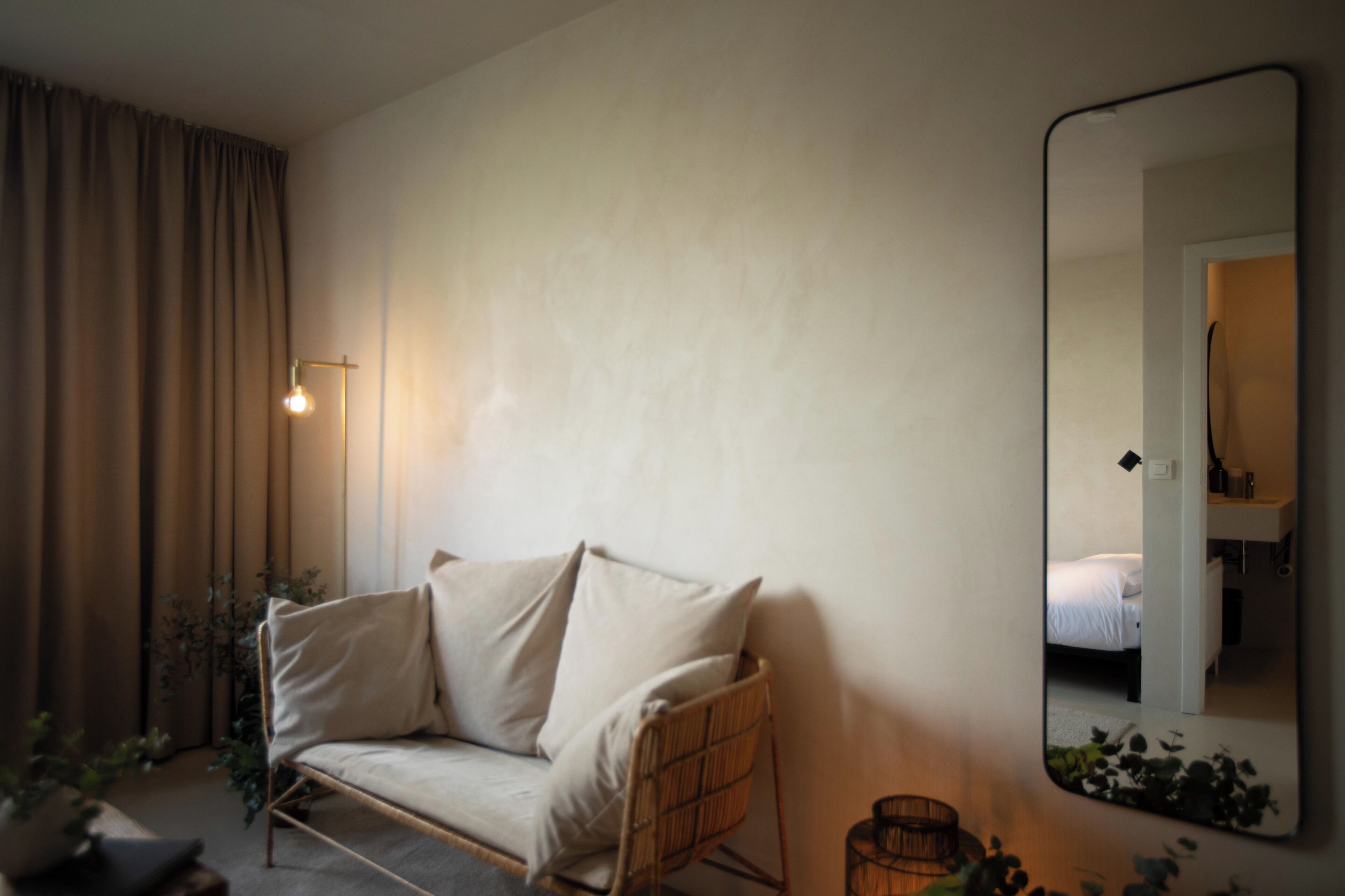 A room with a sofa, a mirror, a lamp, and a bed.