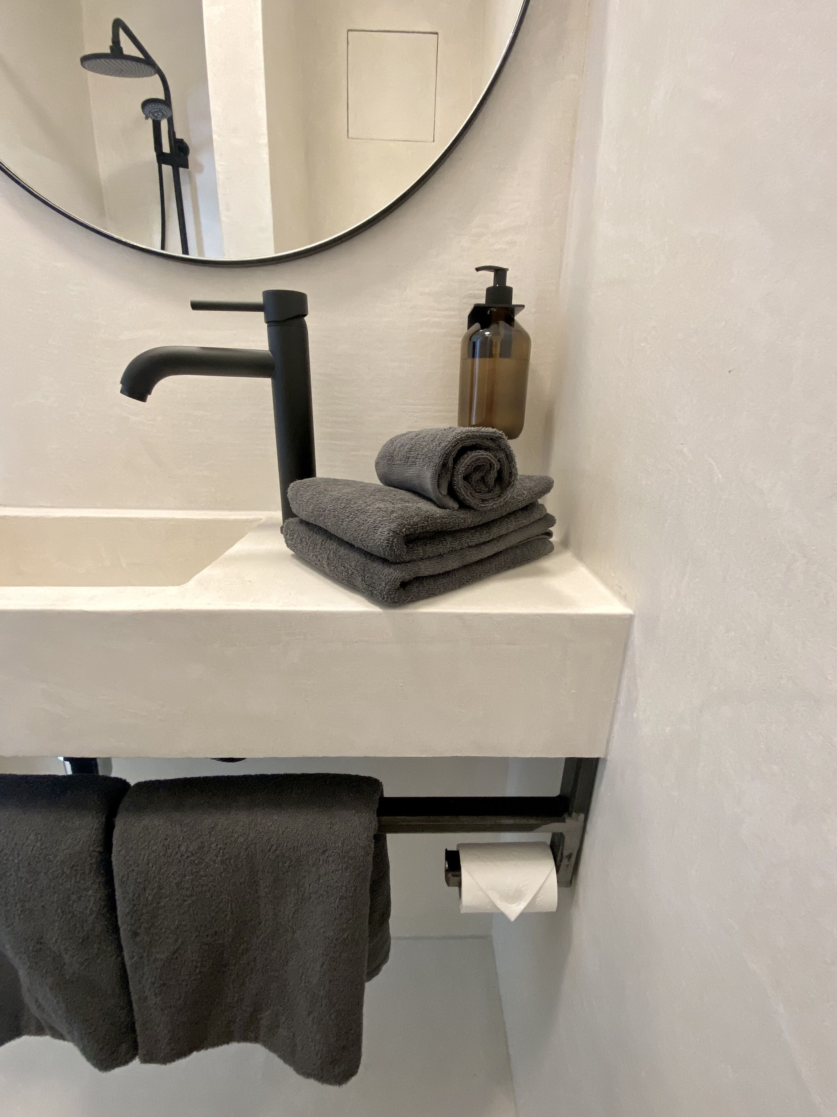 Un bagno con un lavandino bianco, un rubinetto nero e uno specchio. Sul lavandino si trovano una bottiglia di sapone e un asciugamano.