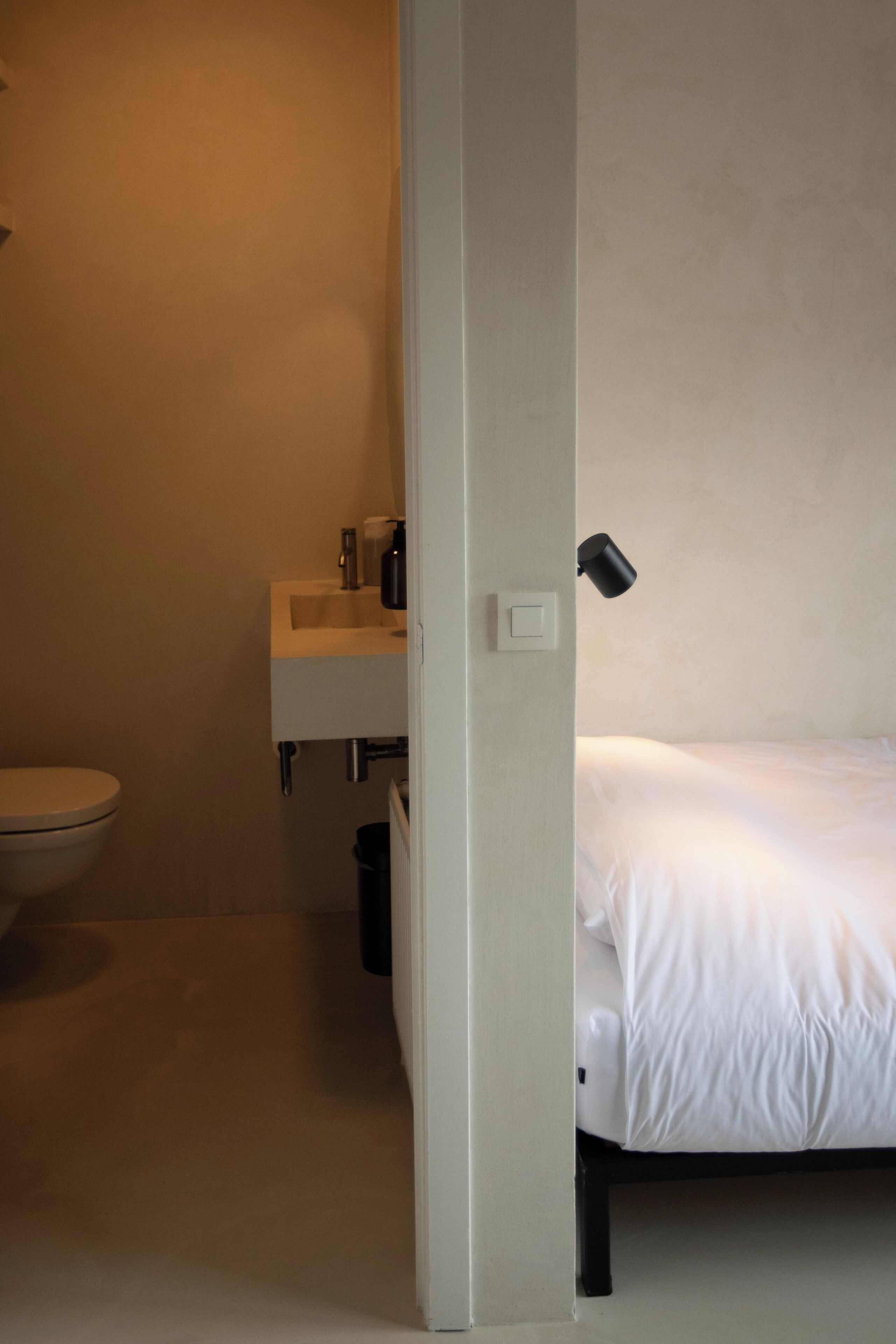 Un baño con inodoro, lavamanos y una cama con ropa blanca.