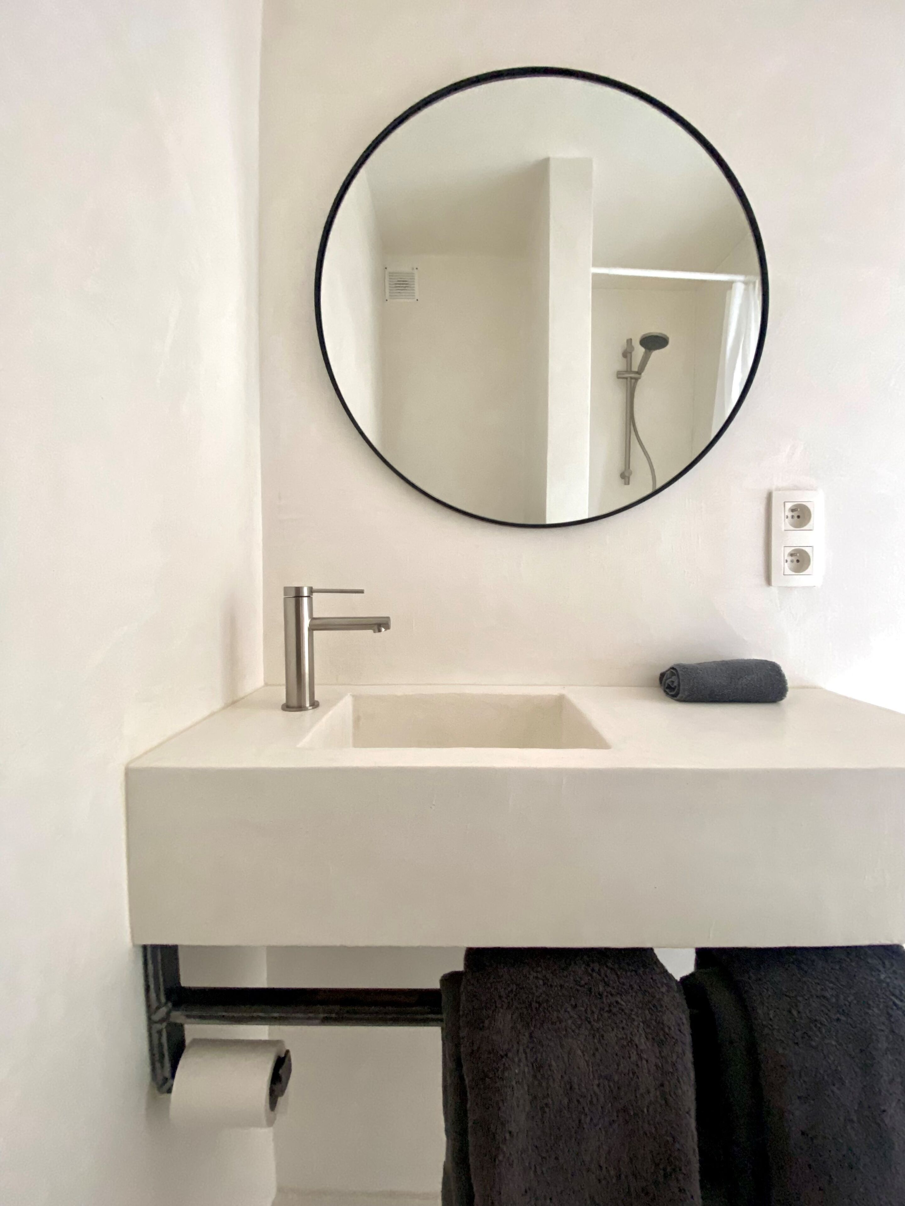 A bathroom with a white sink, a round mirror, a towel, and a toilet paper roll.