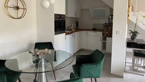 A modern kitchen with white cabinets, a built-in oven, and a microwave. There is a dining area with a glass table and green chairs. - Rheinblick Appartments (Cologne)