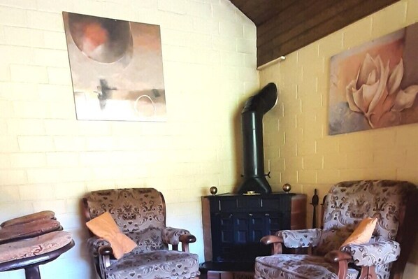 A room with two patterned armchairs, a black wood-burning stove, and a painting of a rose on the wall. - Typ Fuchsbau - Three Bedroom Resort, Sleeps 6 (Bestwig)