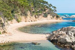 A coastal beach with clear waters, sandy shores, and rocky cliffs.