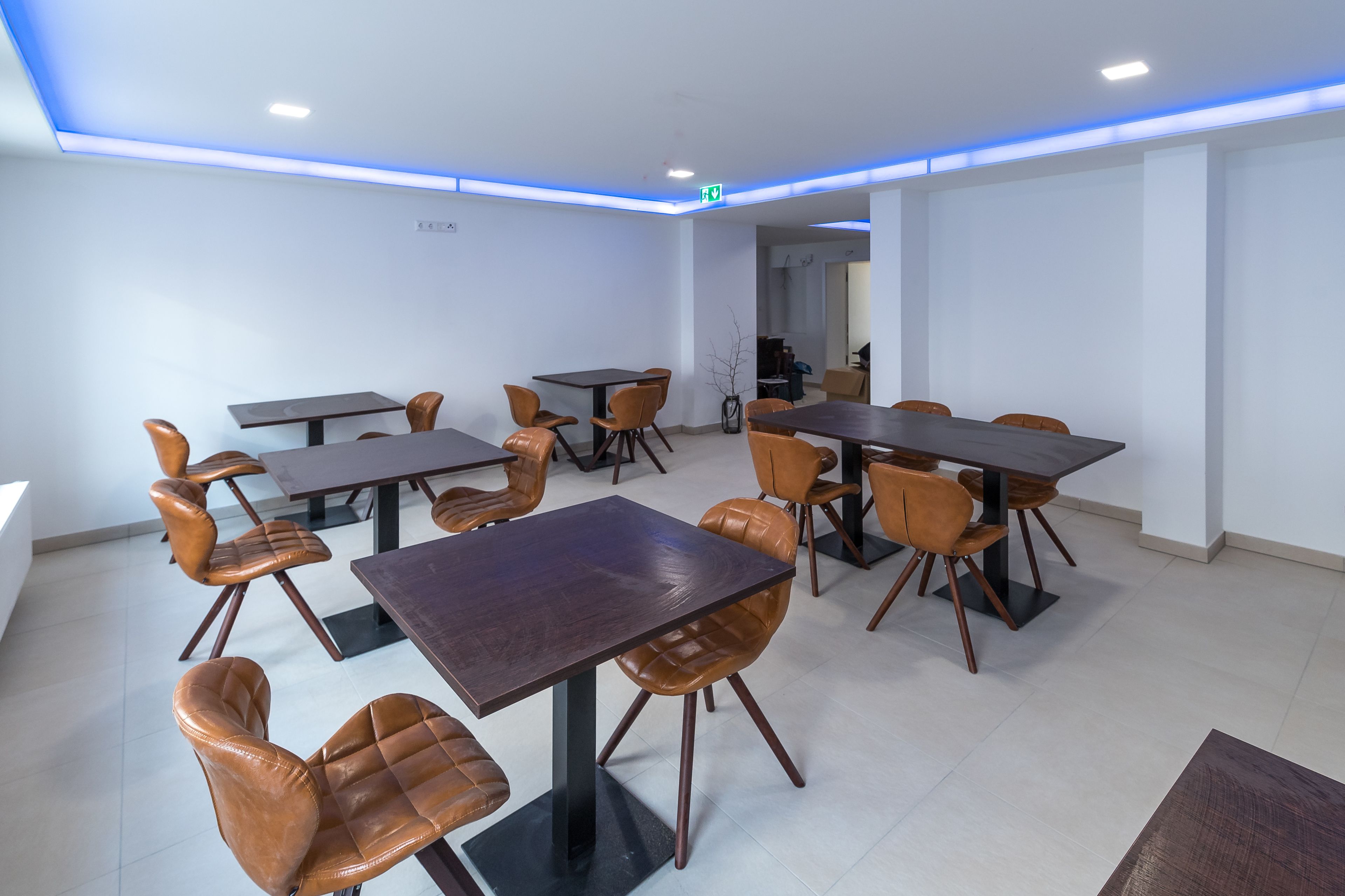 A modern dining area with multiple tables and chairs, a visible exit sign, and a clean, minimalist design.