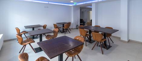 A modern dining area with multiple tables and chairs, a visible exit sign, and a clean, minimalist design.