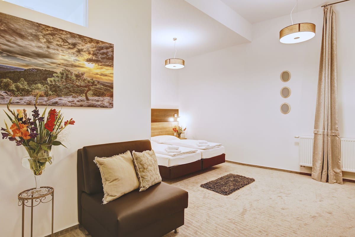 A modern hotel room with a bed, a sofa, a painting, and a vase of flowers.