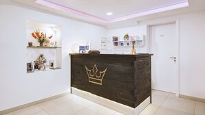 A reception area with a wooden counter featuring a crown emblem, a white door, and a shelf with decorative items. - Boutique-Hotel Kronenstuben (Ludwigsburg)