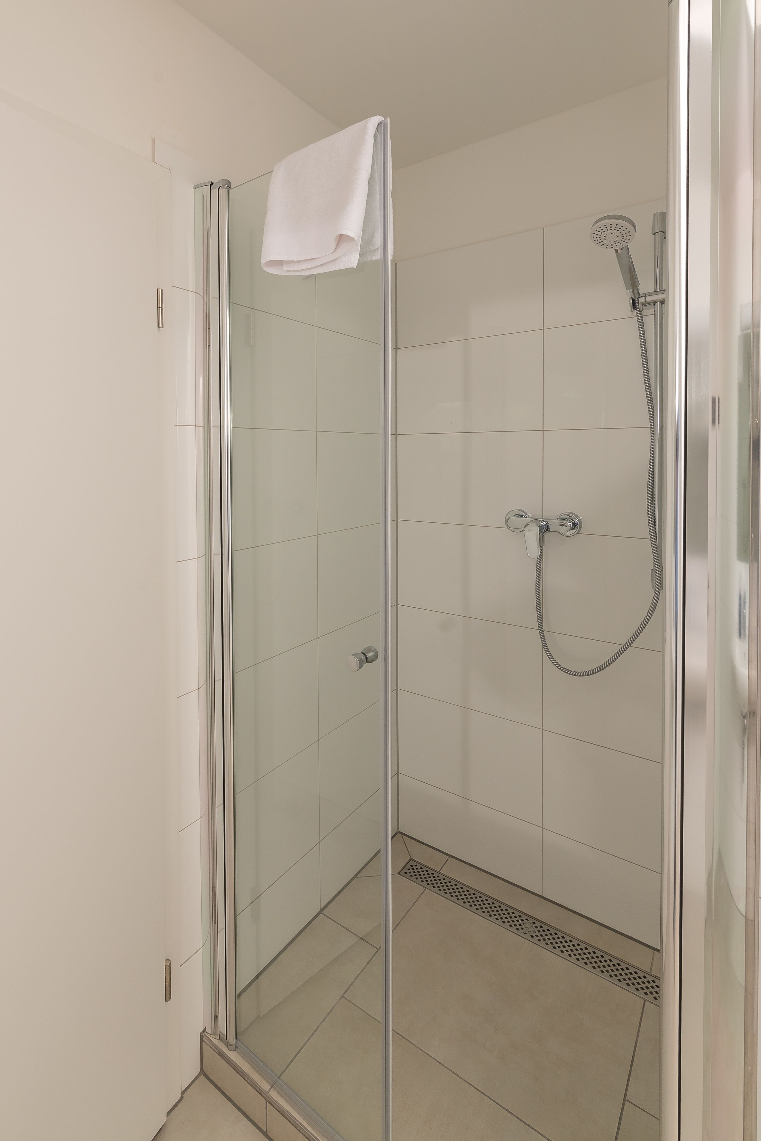A glass-enclosed shower with a handheld showerhead and a towel hanging on the door.