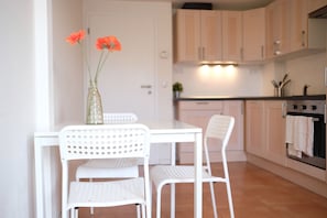 A kitchen with white cabinets, a white table, and two white chairs. There is a vase with flowers on the table. - Legerova apartment (Prague)