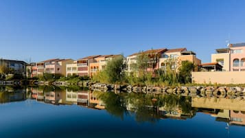 A waterfront residential area with multi-story buildings, a calm water body reflecting the structures, and a clear sky.