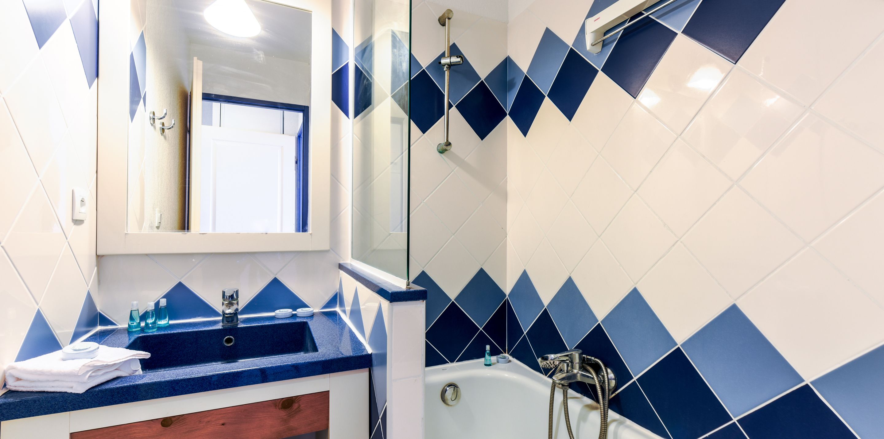 A bathroom with a blue and white tiled wall, a sink with a mirror above it, and a shower area.