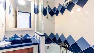A bathroom with a blue and white tiled wall, a sink with a mirror above it, and a shower area.