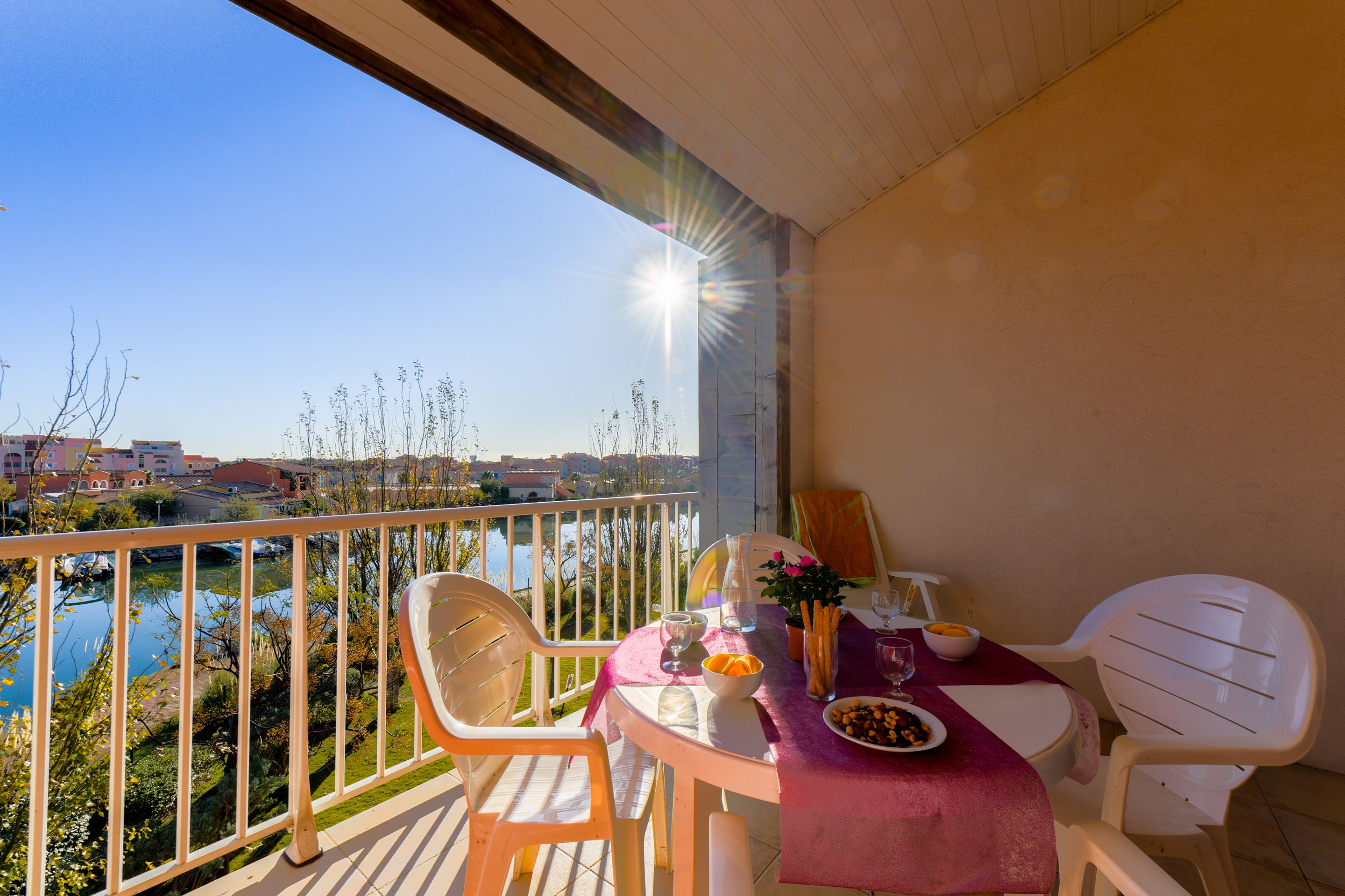 A balcony with a table set for two, overlooking a body of water and buildings.