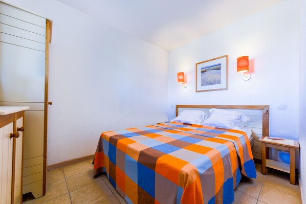 A bedroom with a bed, a nightstand, a wooden dresser, and a framed picture on the wall. - Lagrange Vacances Catalana (Le Barcares)