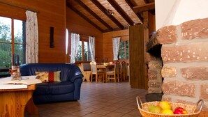 A cozy cabin interior with a dining area, a blue sofa, a wooden table with a book and glass, and a fruit basket. - Haus 2 - Typ B (Blockhaus) (Schönecken)
