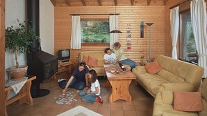A cozy cabin interior with wooden walls, a sofa, a table, and a fireplace. - Haus 2 - Typ B (Blockhaus) (Schönecken)