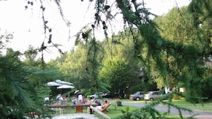 An outdoor seating area with tables and chairs, surrounded by trees and greenery. - Haus 2 - Typ B (Blockhaus) (Schönecken)
