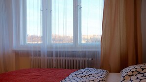 Une chambre à coucher avec un lit, une fenêtre avec des rideaux légers et un radiateur.