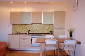 A modern kitchen with wooden cabinets, a tiled backsplash, and a dining area with a table and chairs. - Lannova apartment (Prague)