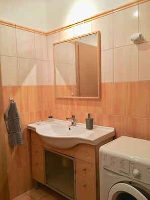 A bathroom with a sink, mirror, towel rack, and a washing machine.