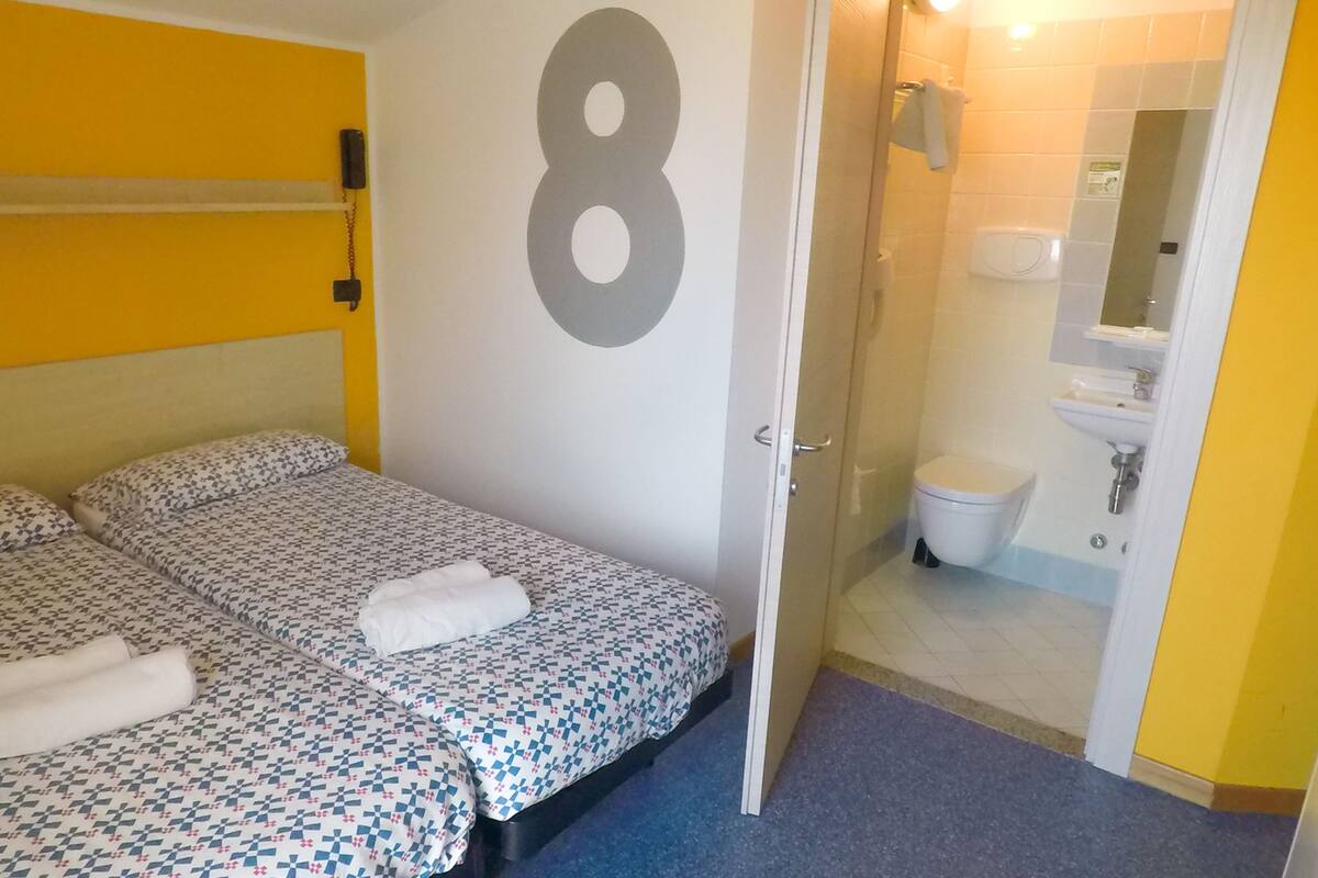 Een kamer met twee bedden, een badkamer met toilet en wastafel, en een groot cijfer 8 op de muur.