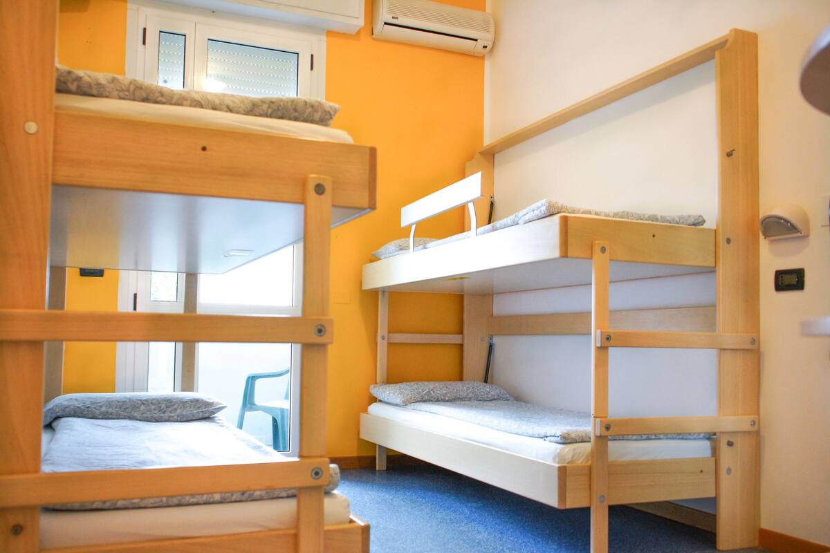 Een kamer met twee stapelbedden, een raam met jaloezieën, een airconditioning en een blauw tapijt.