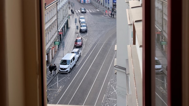 A street view from a window overlooking a city street with buildings, a tram line, and a tower in the background.
