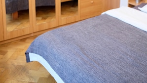 A bedroom with a wooden wardrobe, a bed with a grey blanket, and a small bedside table with a plant.