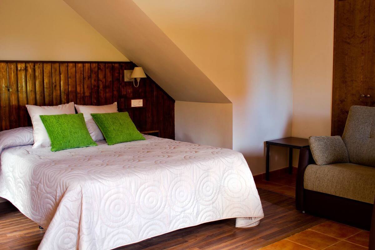 A bedroom with a bed, a chair, a wooden headboard, and a sloped ceiling.