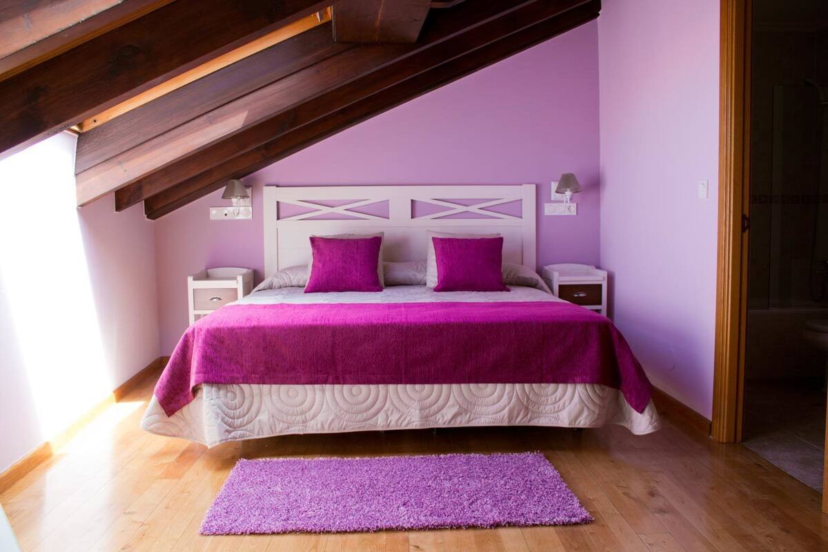 A bedroom with a bed, two nightstands, a purple rug, and a wooden ceiling structure.