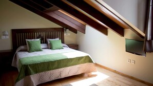 Een slaapkamer met een schuine kap, een bed met groene beddengoed, een wandtelevisie en een houten vloer.