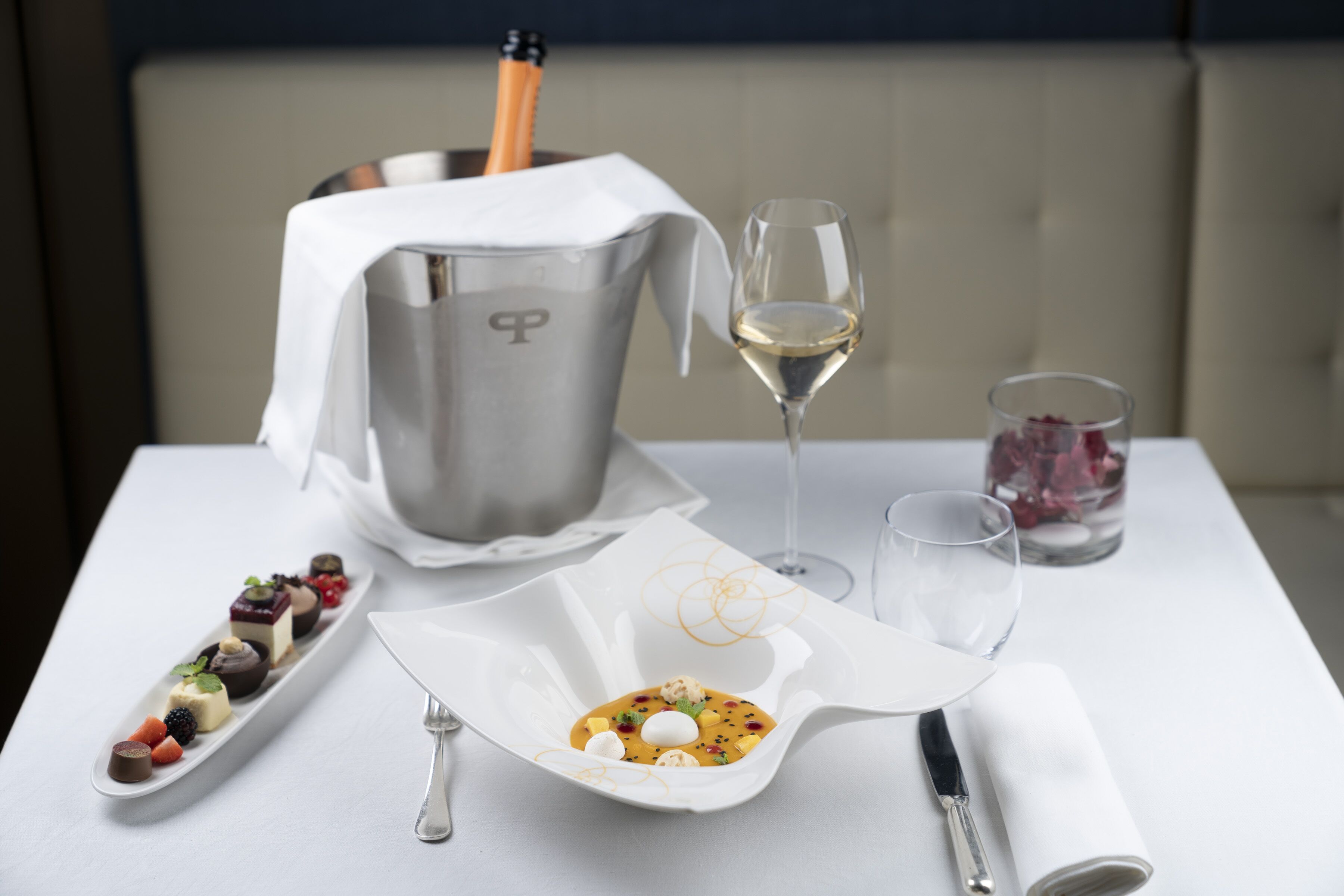 Un tavolo da pranzo con un piatto bianco di dolci assortiti, un bicchiere di vino bianco, una bottiglia di champagne e un bicchiere di vino rosso.