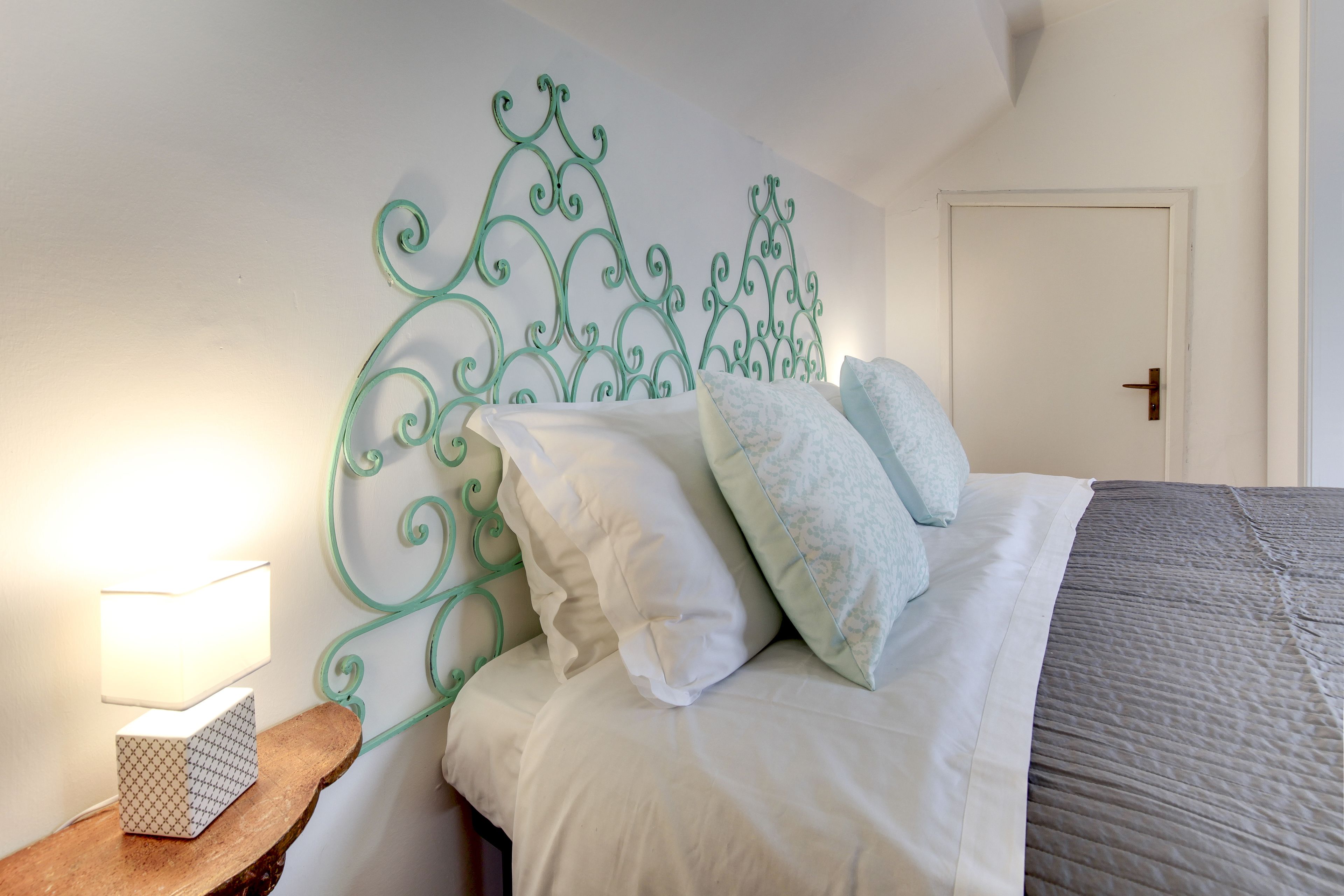 Un lit bien fait, avec une literie blanche et grise, une tête de lit décorative en métal et une table de chevet avec une lampe.
