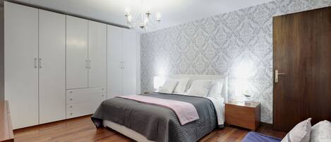 Un dormitorio con cama, mesitas de noche, armario y una puerta.