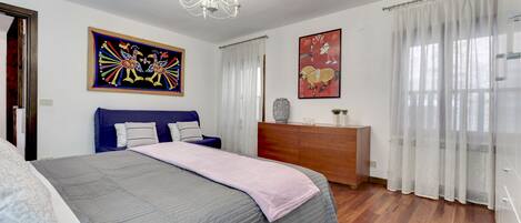 A bedroom with a bed, a dresser, a chandelier, and two wall art pieces.