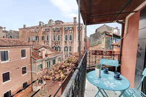 A balcony with a table and chairs, overlooking a courtyard with potted plants and buildings. - Via Garibaldi-Gigli Biennale Terrace by Wonderful Italy (Venice)