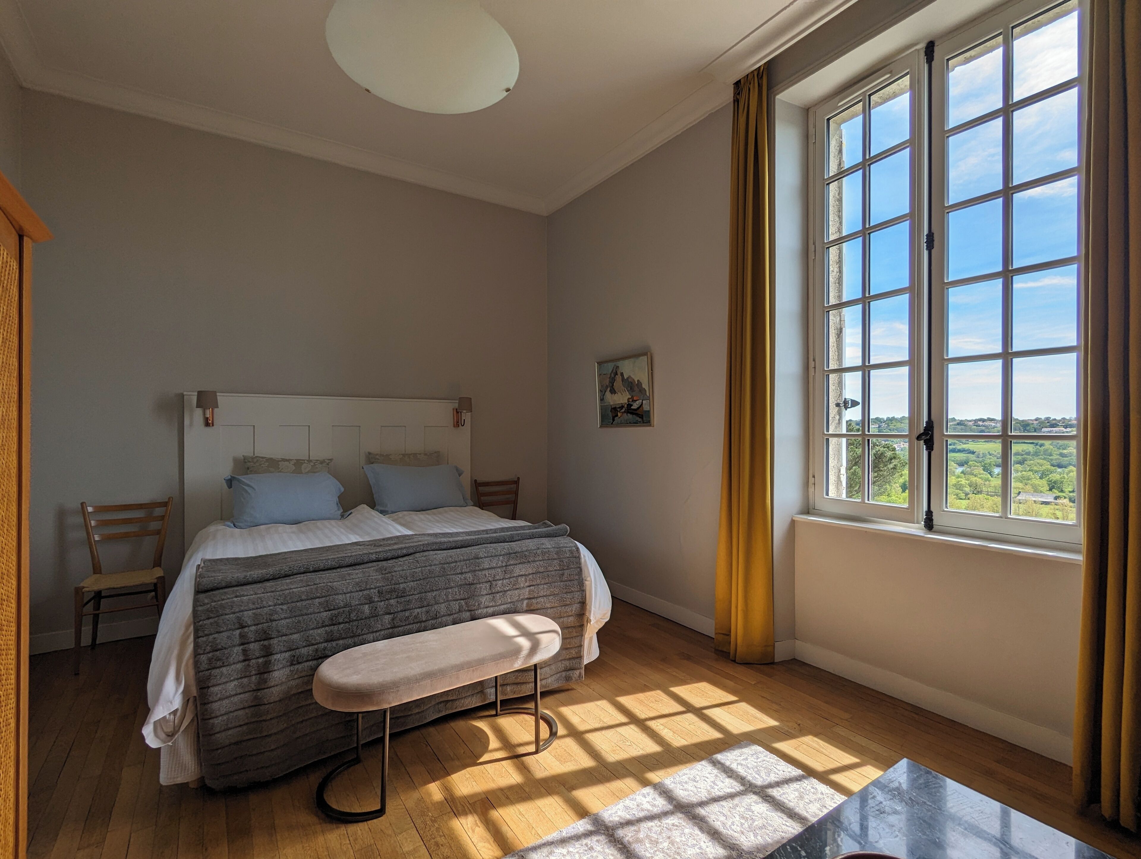 A bedroom with a bed, bench, and large window with curtains.